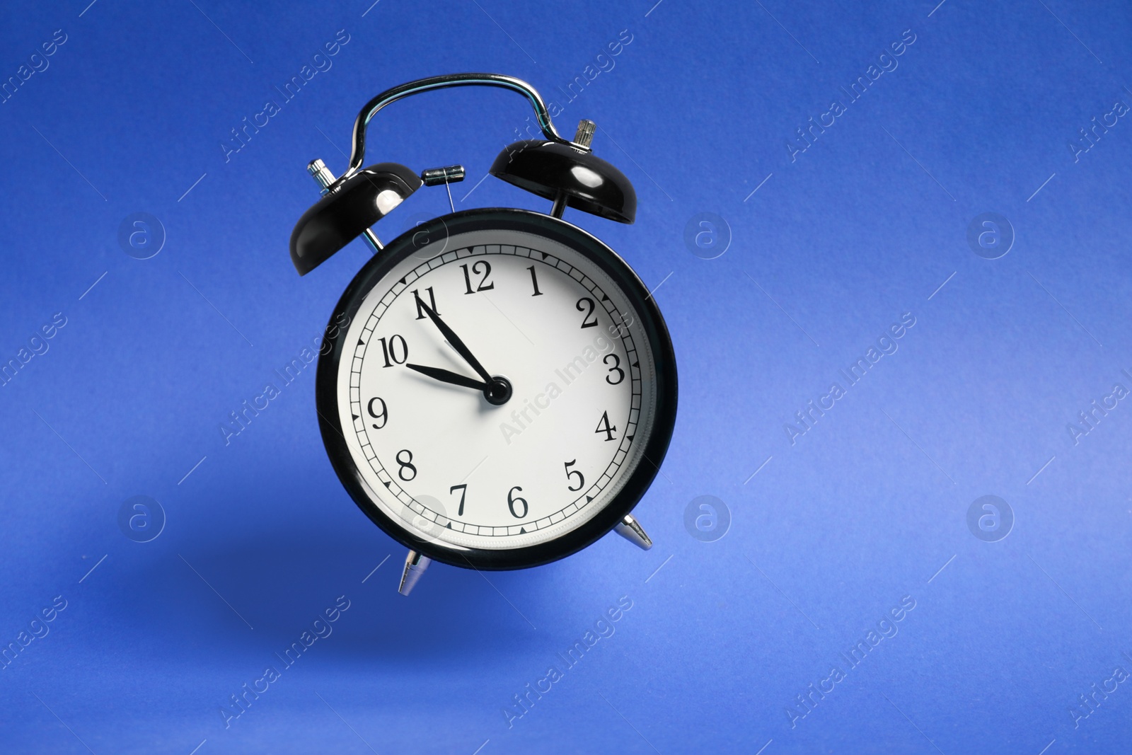 Black alarm clock in air on blue background Photo of Black alarm clock in air on blue background