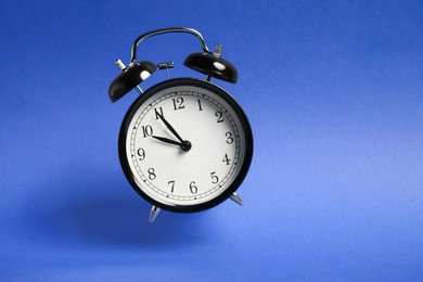 Photo of Black alarm clock in air on blue background