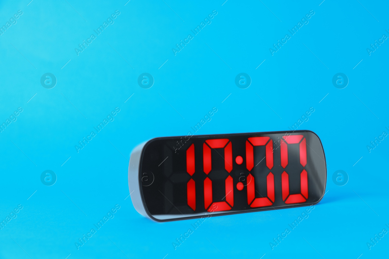Digital alarm clock showing 10:00 o'clock on light blue background, space for text Photo of Digital alarm clock showing 10:00 o'clock on light blue background, space for text