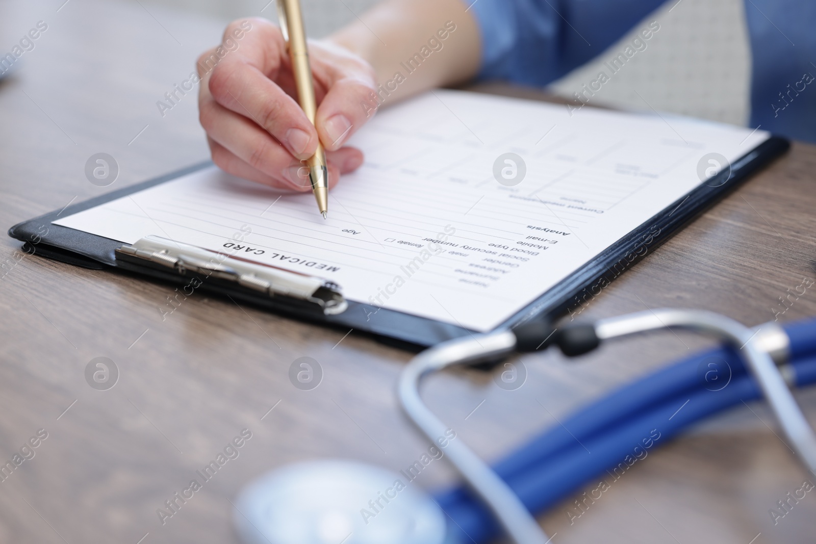 Photo of Doctor filling out patient's medical card at wooden table in clinic, closeup