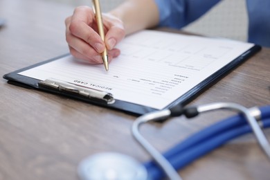 Doctor filling out patient's medical card at wooden table in clinic, closeup