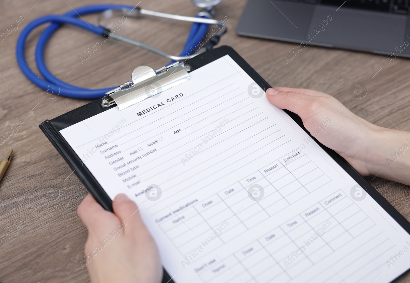 Photo of Doctor holding clipboard with patient's medical card at wooden table, closeup