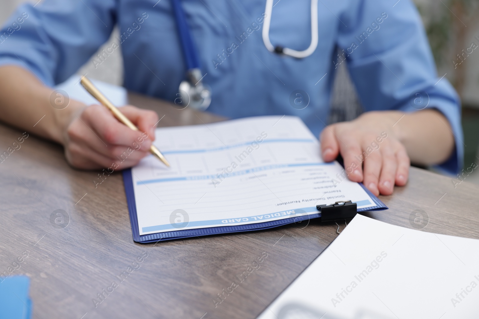 Photo of Doctor filling out patient's medical card at wooden table in clinic, closeup