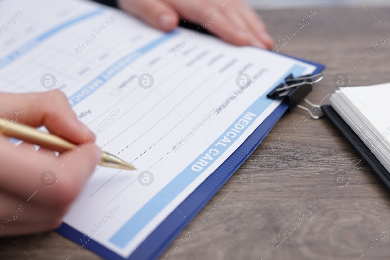 Photo of Doctor filling out patient's medical card at wooden table, closeup