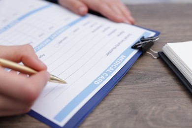 Doctor filling out patient's medical card at wooden table, closeup