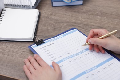 Doctor filling out patient's medical card at wooden table, closeup