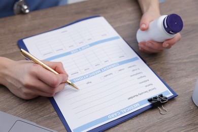 Photo of Doctor with pen and bottle of pills filling out patient's medical card at wooden table, closeup