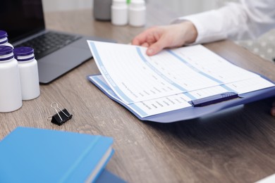 Photo of Doctor holding folder with patient's medical card at wooden table, closeup