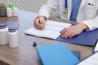 Photo of Doctor filling out patient's medical card at wooden table in clinic, closeup