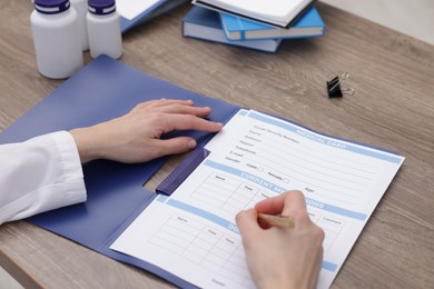 Photo of Doctor filling out patient's medical card at wooden table, closeup