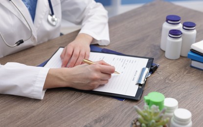 Photo of Doctor filling out patient's medical card at wooden table, closeup