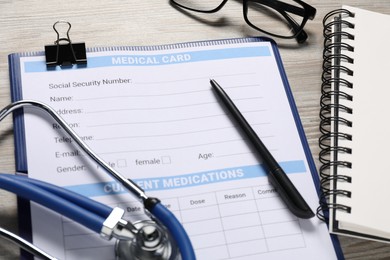 Photo of Medical card form, stethoscope, pen and notepad on wooden table, closeup