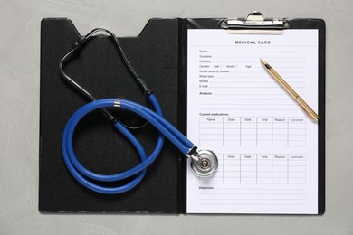 Photo of Medical card form, pen and stethoscope on grey textured table, top view