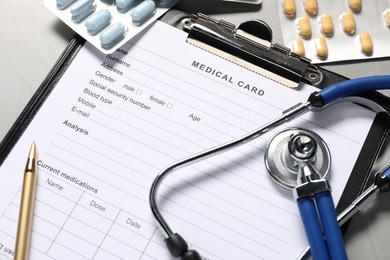 Photo of Medical card form, pen, pills and stethoscope on grey textured table, above view