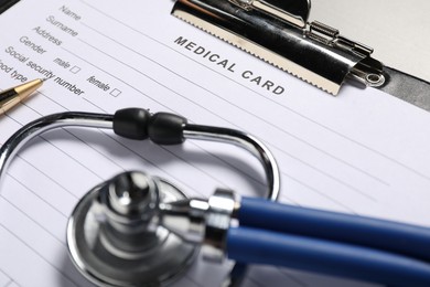 Photo of Medical card form, pen and stethoscope on grey table, closeup