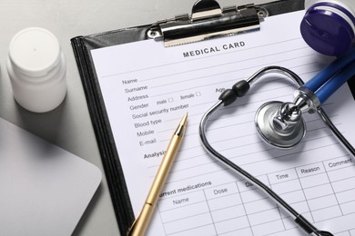 Photo of Medical card form, pen, pills and stethoscope on grey table, above view