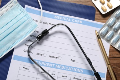 Photo of Flat lay composition with medical card form, pills and stethoscope on wooden table