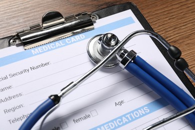 Photo of Medical card form, clipboard and stethoscope on wooden table, closeup