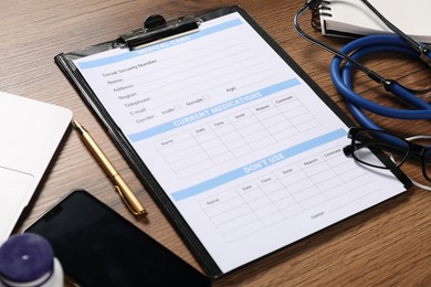 Photo of Medical card form, clipboard, pen and stethoscope on wooden table, closeup