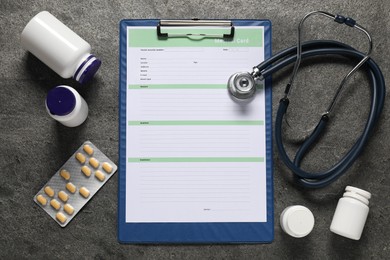 Photo of Medical card form, pills and stethoscope on grey textured table, flat lay