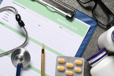 Photo of Flat lay composition with medical card form, pills and stethoscope on grey textured table