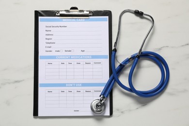 Photo of Medical card form and stethoscope on white marble table, flat lay