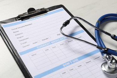 Photo of Medical card form and stethoscope on white marble table, closeup