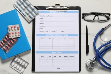 Photo of Medical card form, pen, pills, glasses and stethoscope on white marble table, flat lay