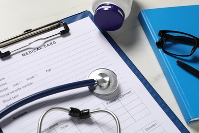 Photo of Medical card form, stethoscope and pills on white table, closeup