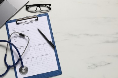 Photo of Medical card form, pen, glasses and stethoscope on white marble table, flat lay. Space for text