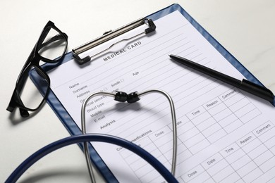 Photo of Medical card form, pen, glasses and stethoscope on white table, closeup