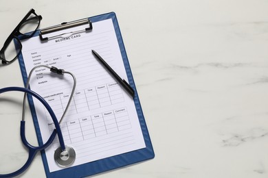 Photo of Medical card form, pen, glasses and stethoscope on white marble table, flat lay. Space for text