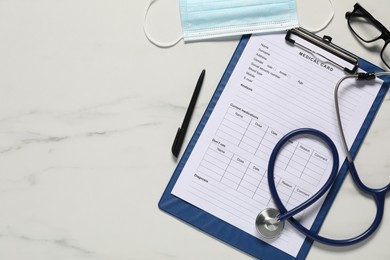 Photo of Medical card form, pen, protective mask and stethoscope on white marble table, flat lay. Space for text