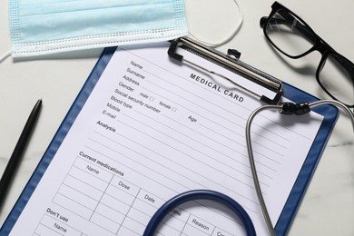 Photo of Medical card form, pen, protective mask and stethoscope on white marble table, flat lay