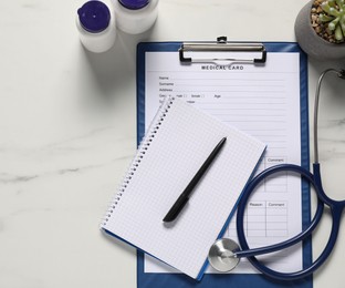 Photo of Medical card form, pen, notepad and stethoscope on white marble table, flat lay