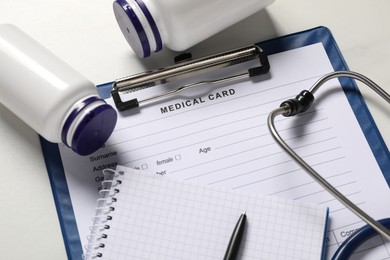 Photo of Medical card form, pen, notepad, pills and stethoscope on white table, above view