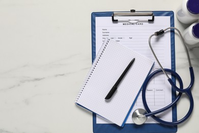 Photo of Medical card form, pen, notepad and stethoscope on white marble table, flat lay. Space for text