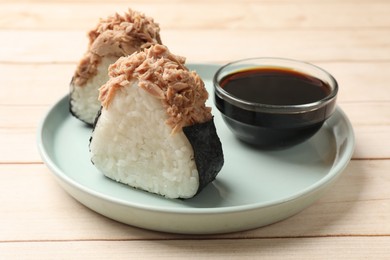 Photo of Tasty onigiri (Japanese rice balls) with tuna and soy sauce on wooden table, closeup