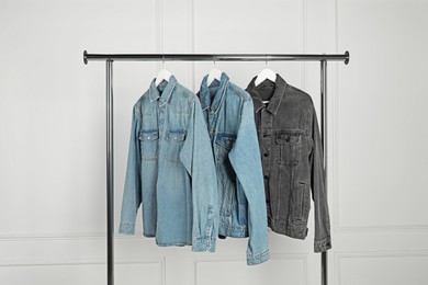 Photo of Many stylish denim jackets hanging from rack near white wall