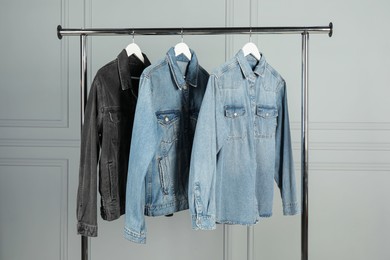 Photo of Many stylish denim jackets hanging from rack near white wall