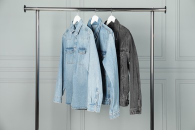 Photo of Many stylish denim jackets hanging from rack near white wall