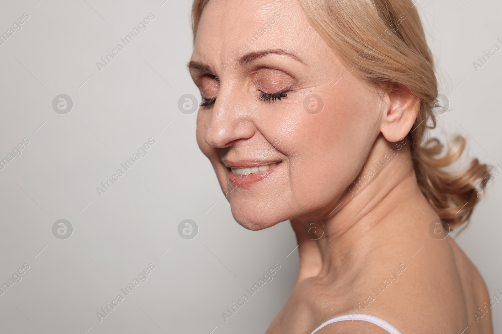 Photo of Smiling middle aged woman on grey background. Space for text