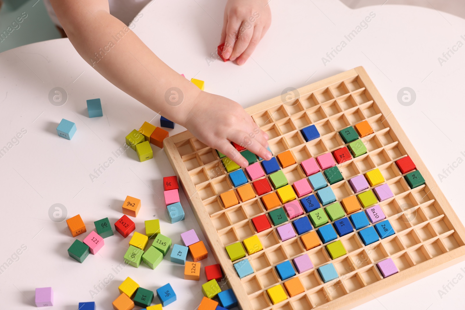 Photo of Motor skills development. Little boy playing with Times table tray at white table, above view