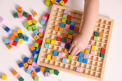 Photo of Motor skills development. Little boy playing with Times table tray at white table, top view