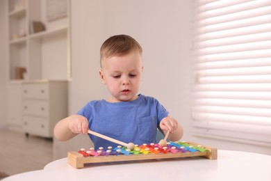 Photo of Motor skills development. Little boy playing with xylophone at white table indoors