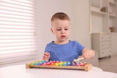 Photo of Motor skills development. Little boy playing with xylophone at white table indoors