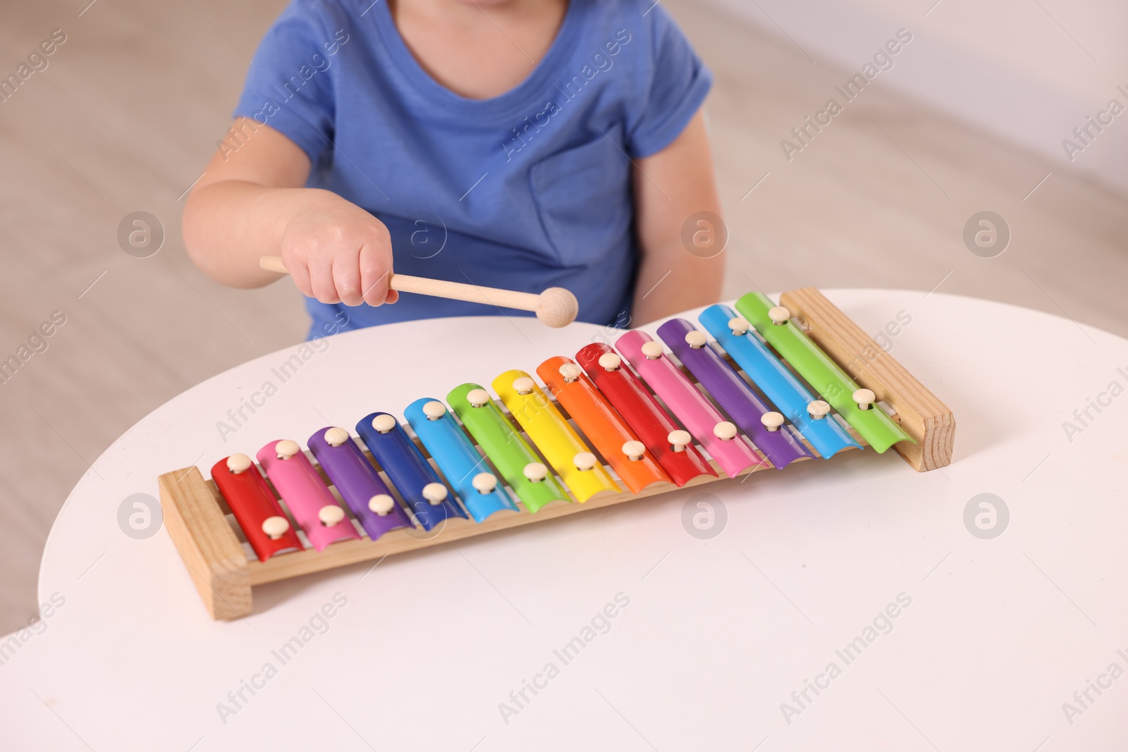 Photo of Motor skills development. Little boy playing with xylophone at white table indoors, closeup