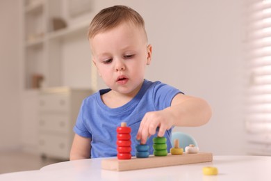 Photo of Motor skills development. Little boy playing with stacking toy at white table indoors