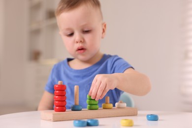 Photo of Motor skills development. Little boy playing with stacking toy at white table indoors, selective focus