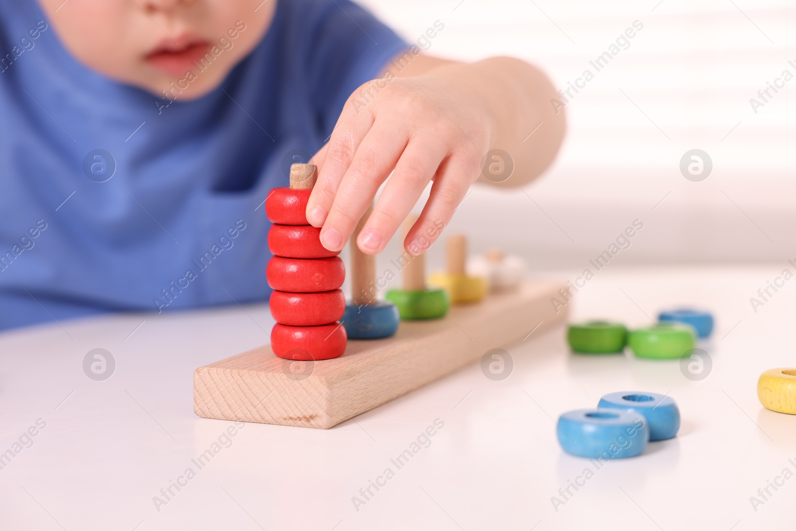 Photo of Motor skills development. Little boy playing with stacking toy at white table indoors, closeup